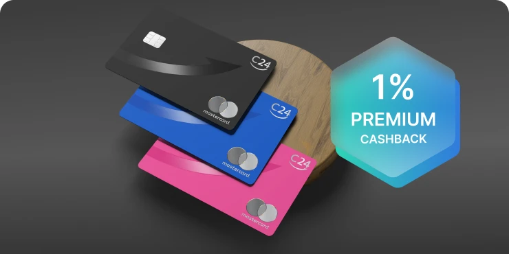 Drei verschieden farbige metallische C24 Mastercard Karten liegen auf einem runden Holzbrett. Die Farben sind Schwarz, Dunkelblau und Pink.